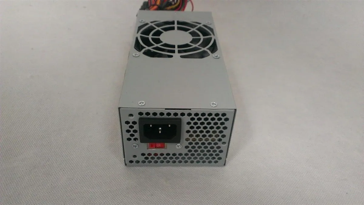 Compact TFX power supply unit, matte metal casing, 80mm fan visible, standard cable bundle attached