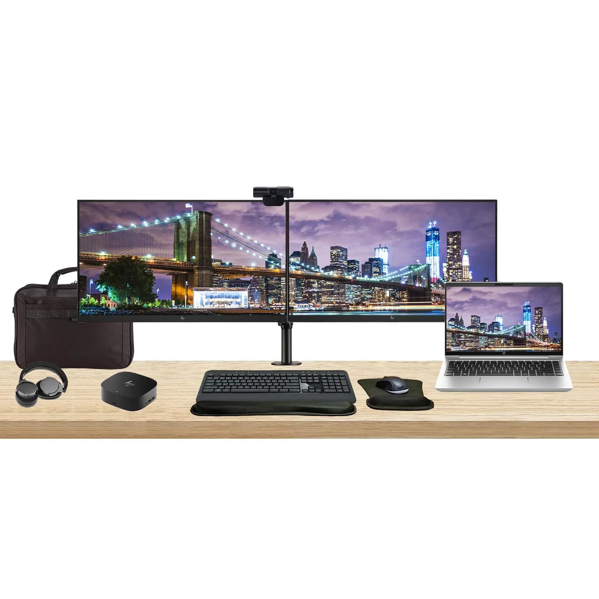 Closed silver 14-inch laptop beside two 24-inch monitors on a dual desk stand with dock keyboard mouse webcam headphones gel rest