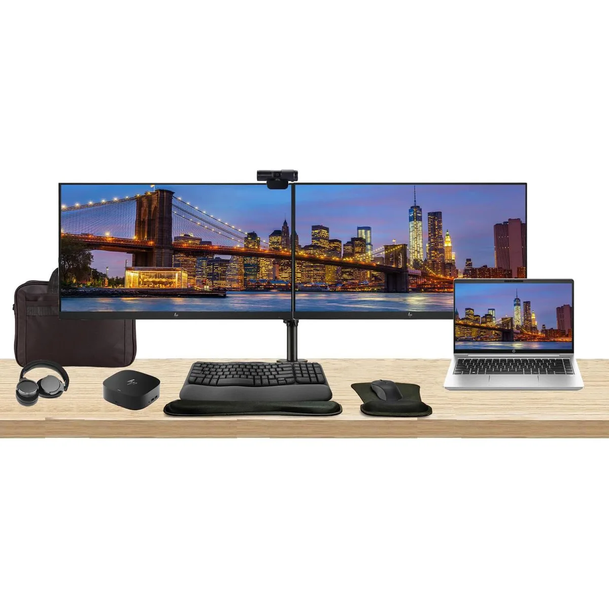 A silver 14-inch laptop beside two 27-inch monitors on a dual stand with a USB-C dock, wireless keyboard and mouse, webcam