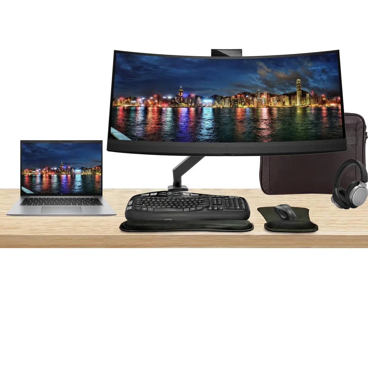 A silver 14 inch laptop, a curved 34 inch monitor on a desk mount, wireless keyboard, mouse, headphones and a briefcase
