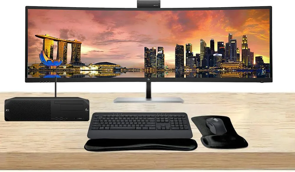 Compact silver desktop tower beside 49-inch curved ultrawide monitor with wireless keyboard and mouse