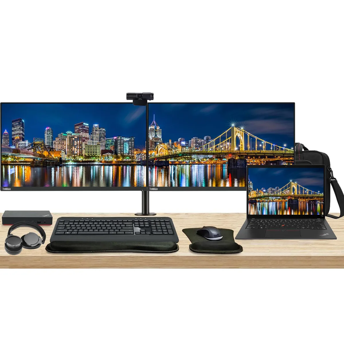 Open laptop beside two monitors on a shared stand with dock keyboard mouse webcam headphones bag