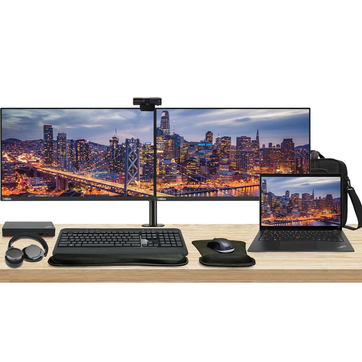 Closed black 14 inch ThinkPad laptop beside two 27 inch monitors on a dual stand with keyboard, mouse, webcam, headphones and briefcase