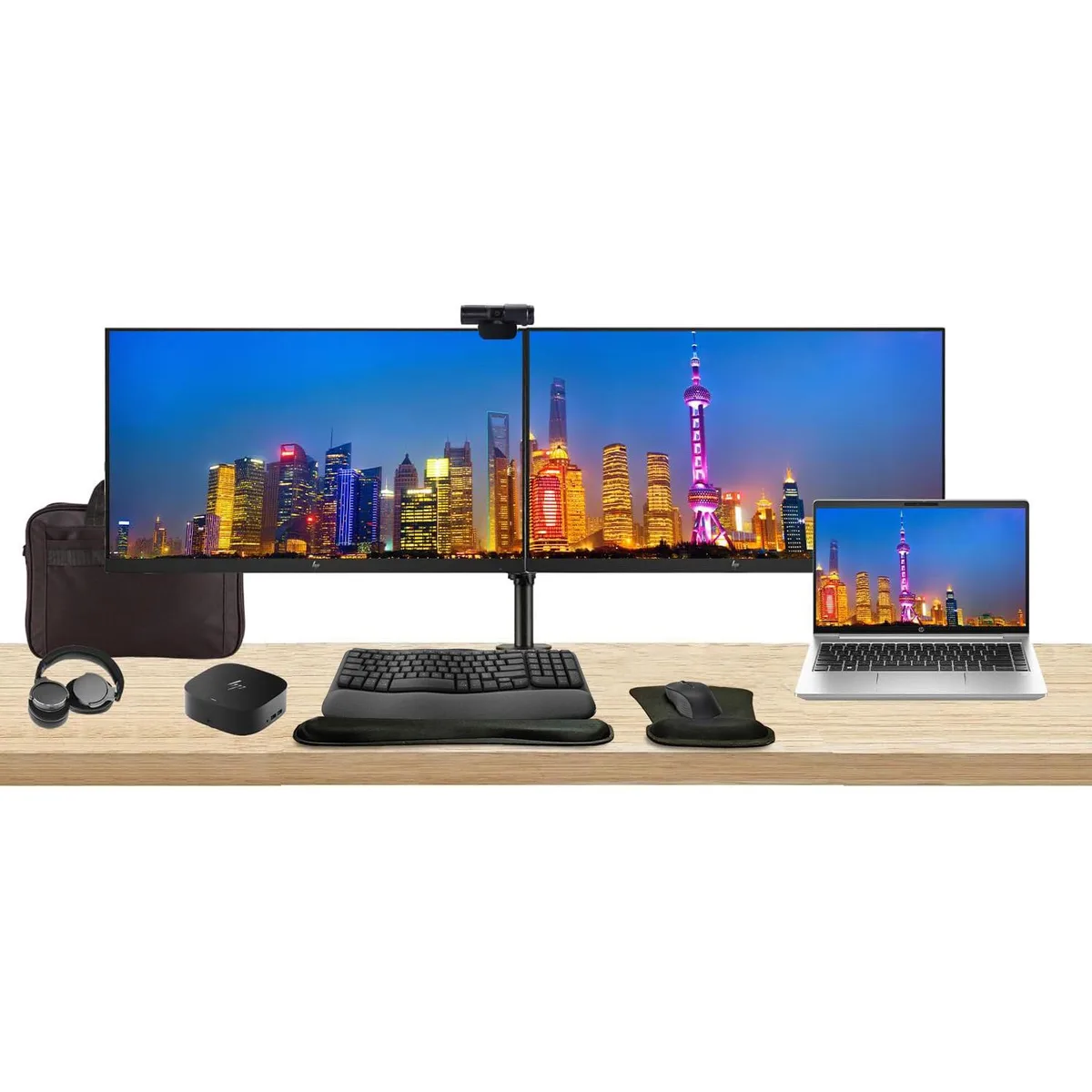 Open laptop beside two monitors on a shared stand, plus dock, keyboard, mouse, webcam, headphones and bag