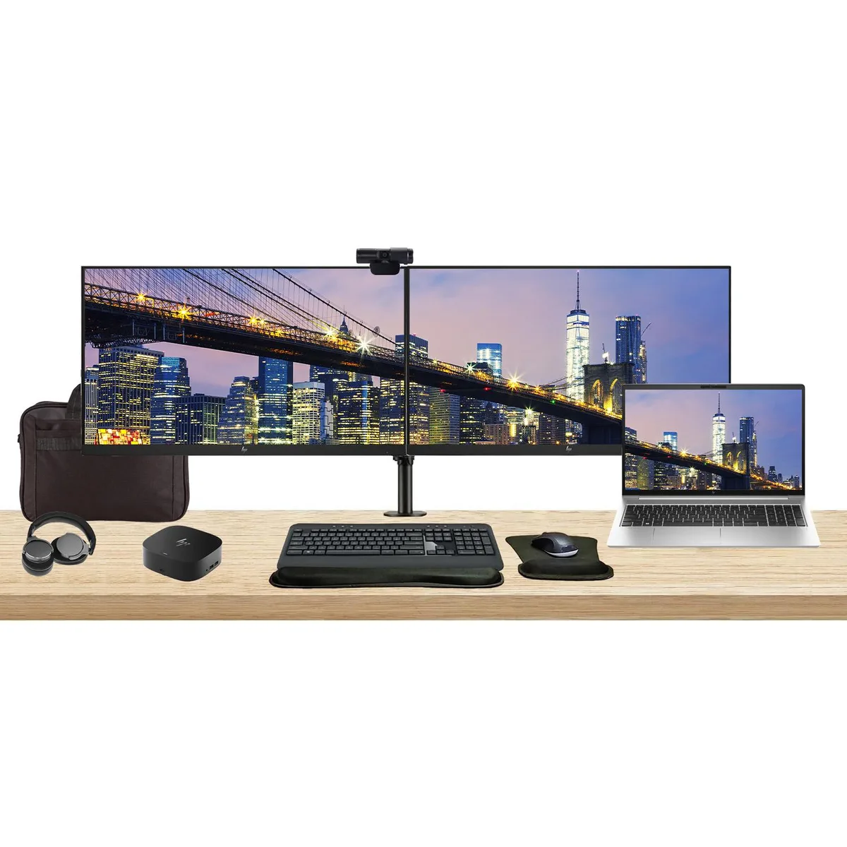 Silver laptop open beside two black 27 inch monitors on a dual clamp stand with wireless keyboard mouse webcam headphones gel rest