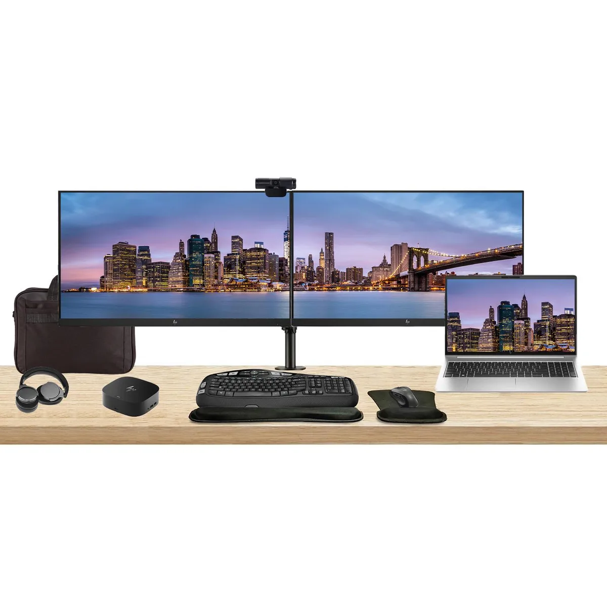 Silver laptop open beside two 27 inch monitors on a dual stand with dock keyboard mouse webcam headphones and bag