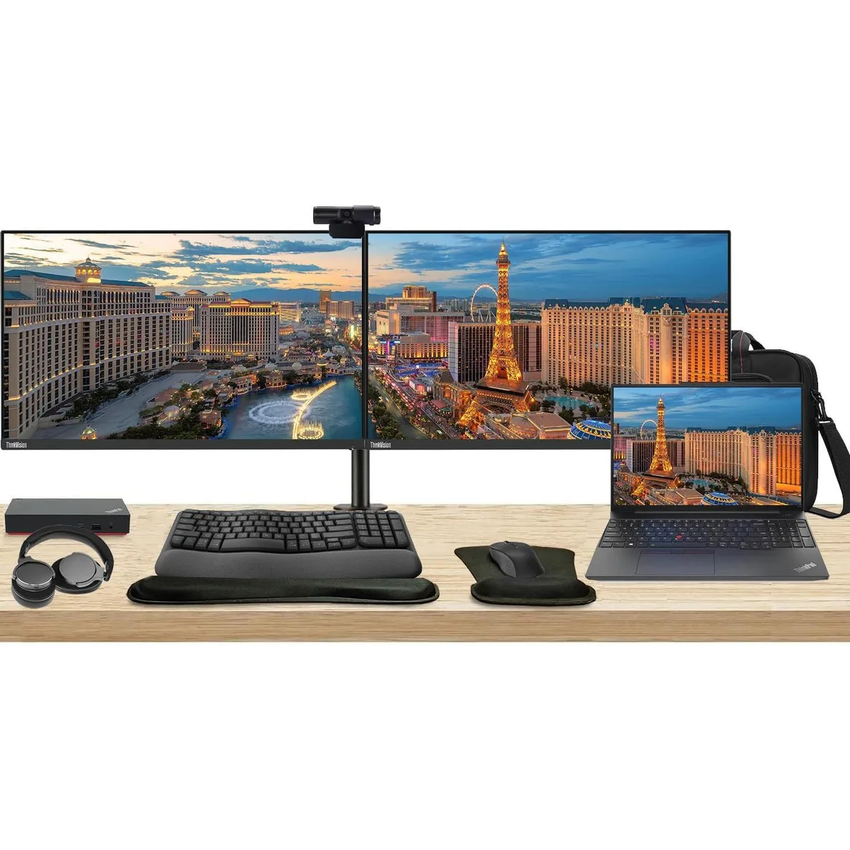 Open laptop beside two 27 inch monitors on a dual stand with dock keyboard mouse webcam headphones bag and wrist rest