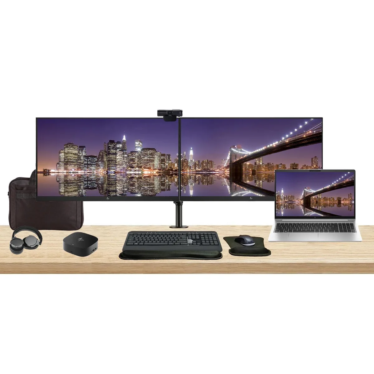 Silver laptop beside two 27 inch monitors on a dual stand with dock keyboard mouse webcam headphones and bag