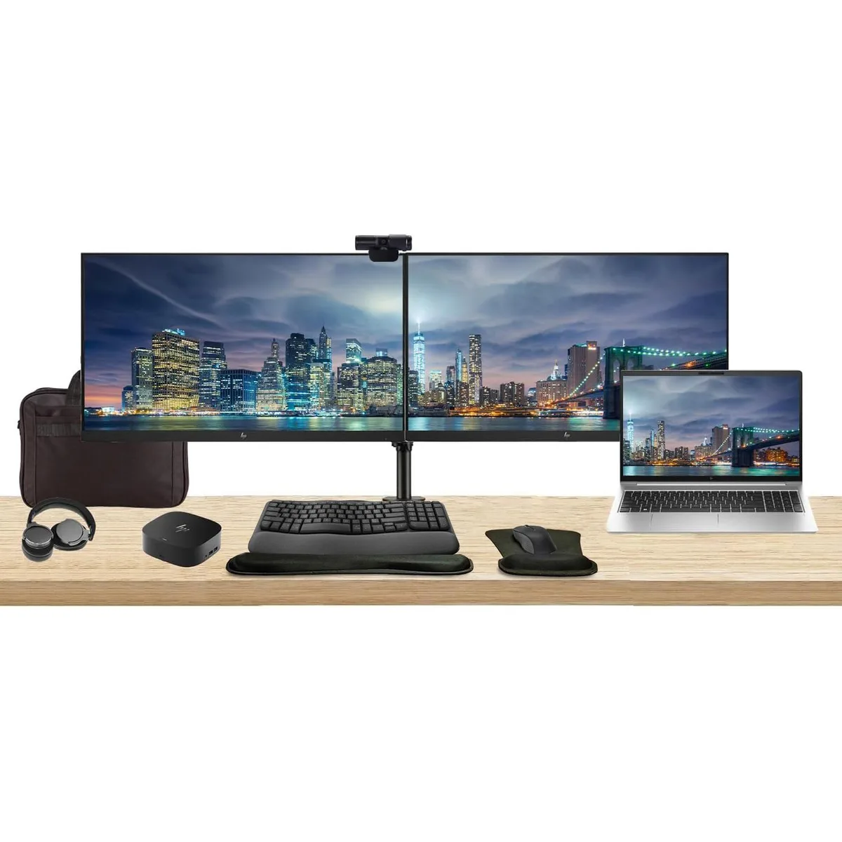 Silver laptop beside two 27 inch monitors on a dual stand with dock keyboard mouse webcam headphones gel pad and briefcase