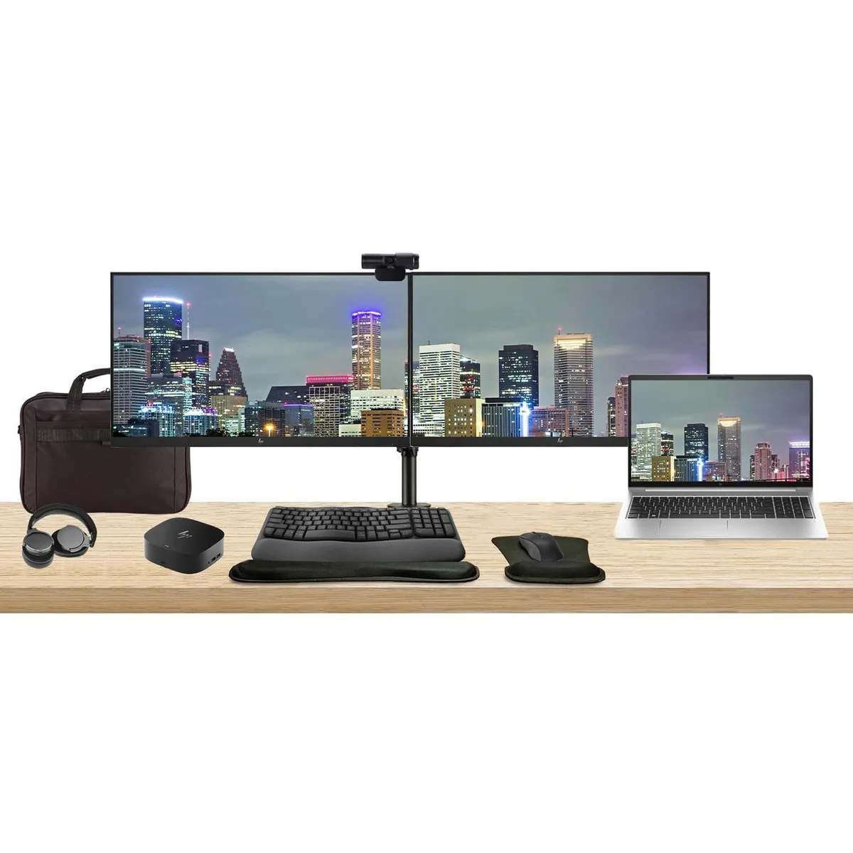 Open laptop beside two monitors on a dual arm stand with dock keyboard mouse webcam headphones bag