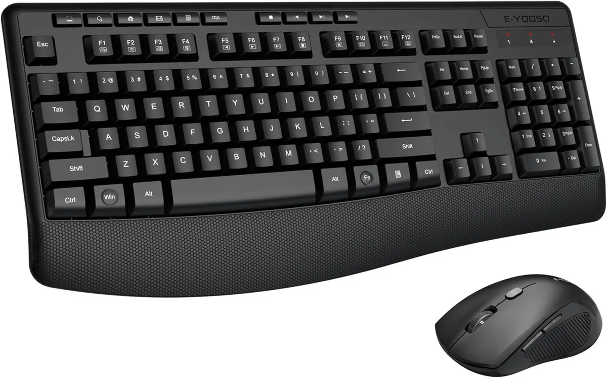 Black full-size wireless keyboard with wrist rest and matching mouse on desk