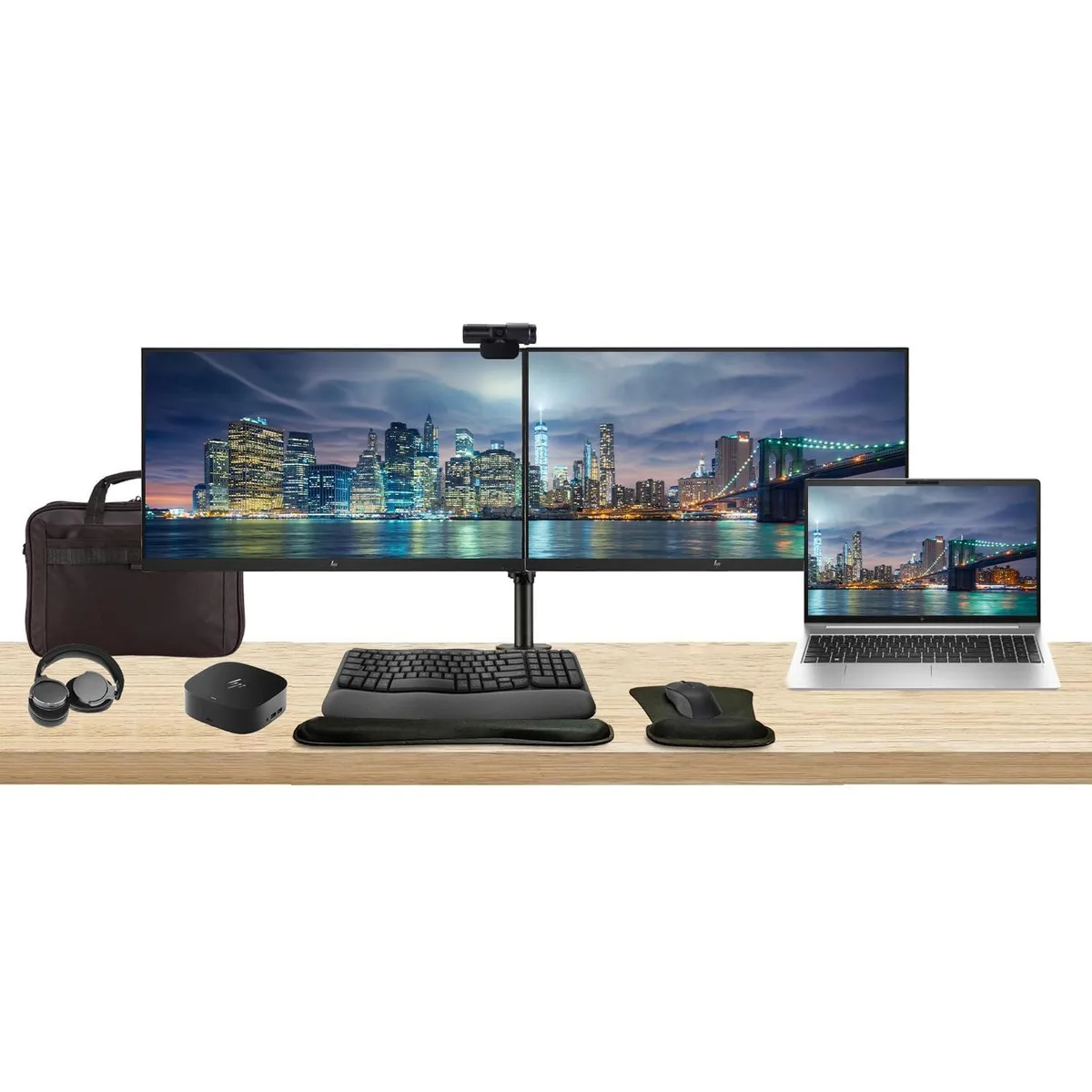 Silver laptop open beside two black monitors on a dual-arm stand, with dock, keyboard, mouse, webcam, headphones