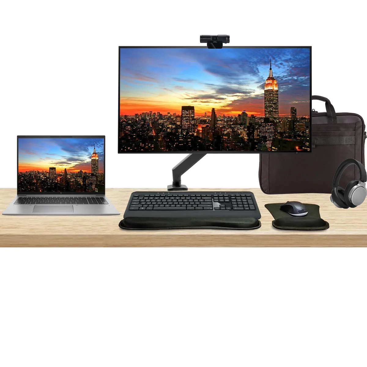 Open 16 inch silver laptop beside 32 inch 4K monitor on desk mount with keyboard mouse webcam headphones and briefcase