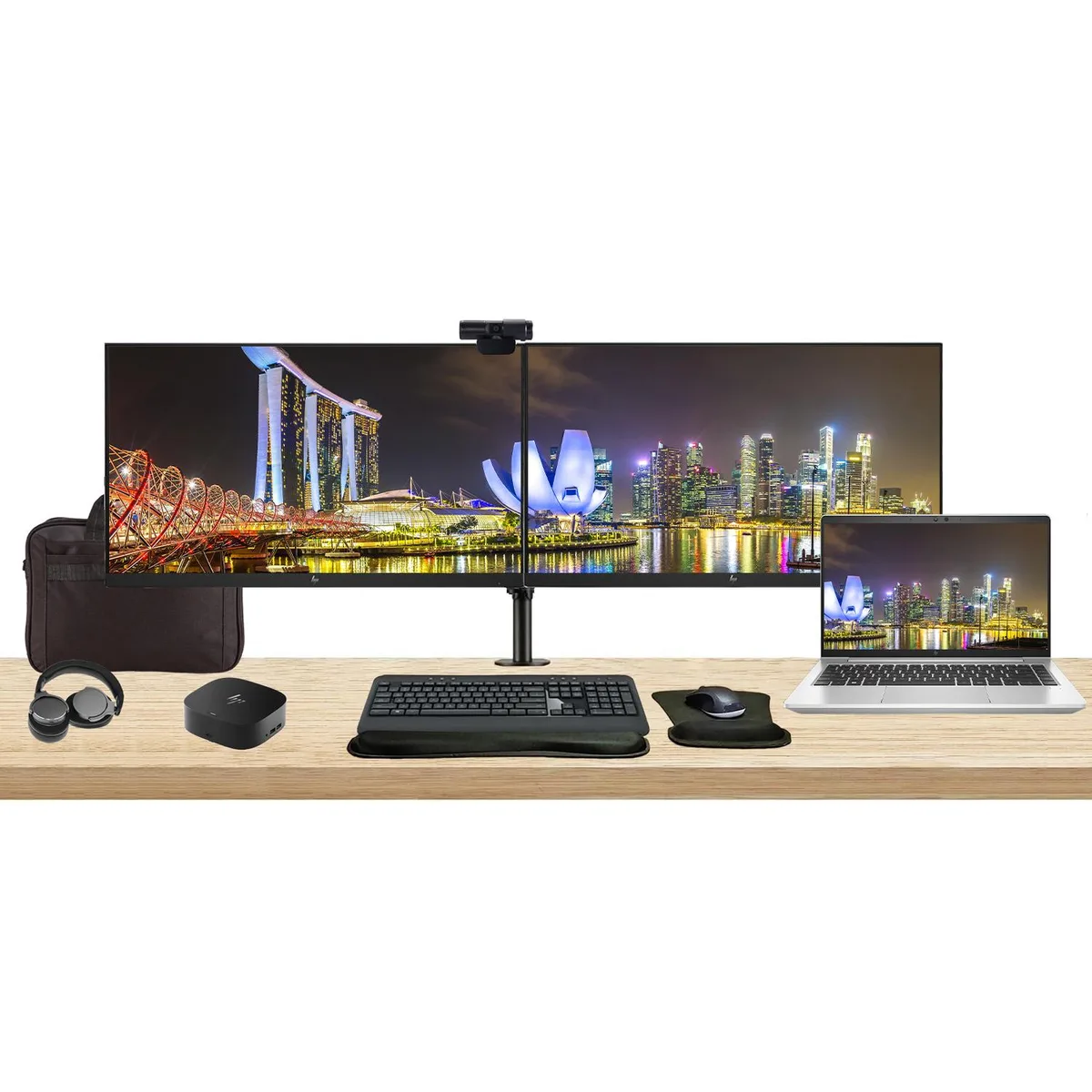 Open laptop beside two monitors on a dual stand with dock, keyboard, mouse, webcam, headphones and bag